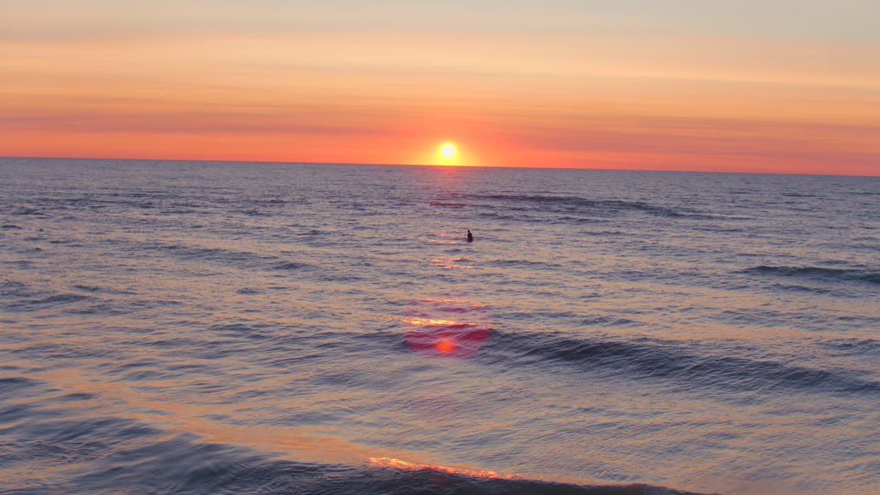 Beautiful sunrise over Lake Michigan with a surfer floating in gentle waves, waiting for the perfect set as golden morning light glows across the horizon and rolling water