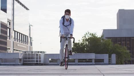 hombre asiático con máscara facial montando en bicicleta en el techo del parque corporativo