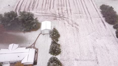 slow motion top view of the snowy farmland in southeast michigan with building, trees and land frozen in snow in usa