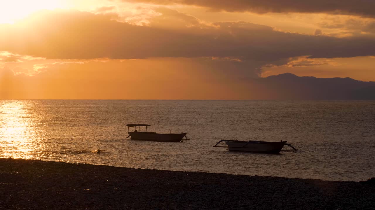 동티모르 의 수도 인  ⁇ 리 에서 아름다운 황금 하늘 의 일몰 을 보면서 바다 에서 수영 하고 있는 사람
