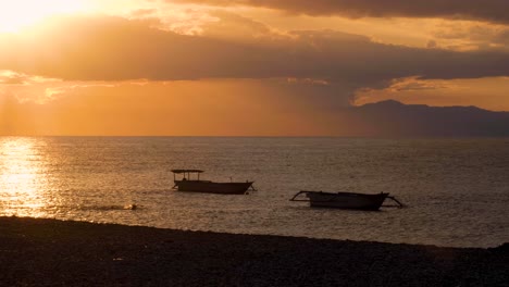 person swimming in the ocean to moored fishing boats during beautiful golden sky sunset in capital dili, east timor timor-leste