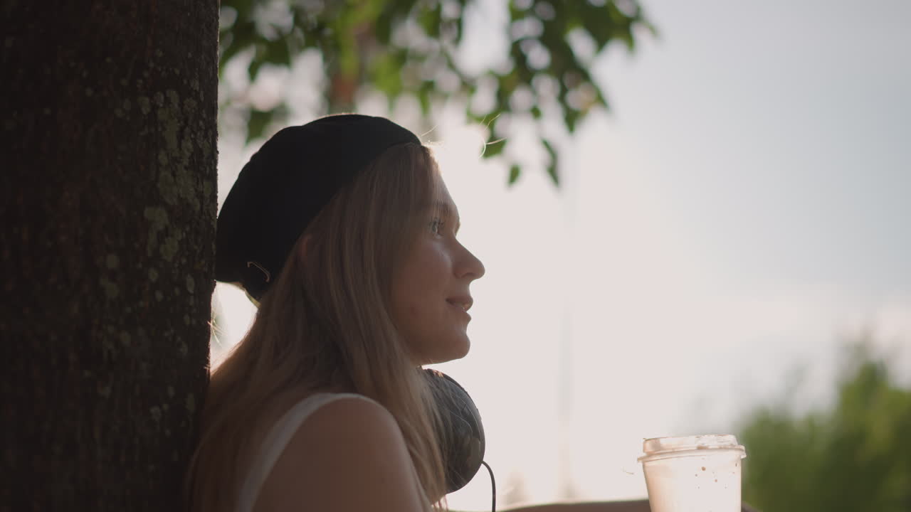 Ragazza che si rilassa all'aperto, donna che si gode un parco soleggiato, signora con le cuffie in un'atmosfera tranquilla del parco, donna che si gode un momento sereno all'aperto sotto la calda luce del sole con le cuffie e un ambiente piacevole