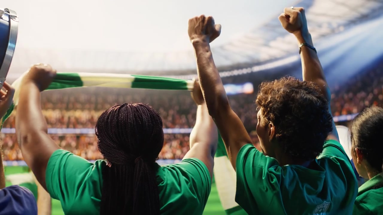 Torcedores de futebol com camisas verdes agitando cachecóis e batendo tambor no estádio.