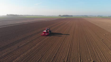 drone shot of red tractor plowing brown, earthy, dutch farmland in vertical lines