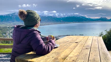 asian woman eats lunch at picnic table on sunny day with ocean view