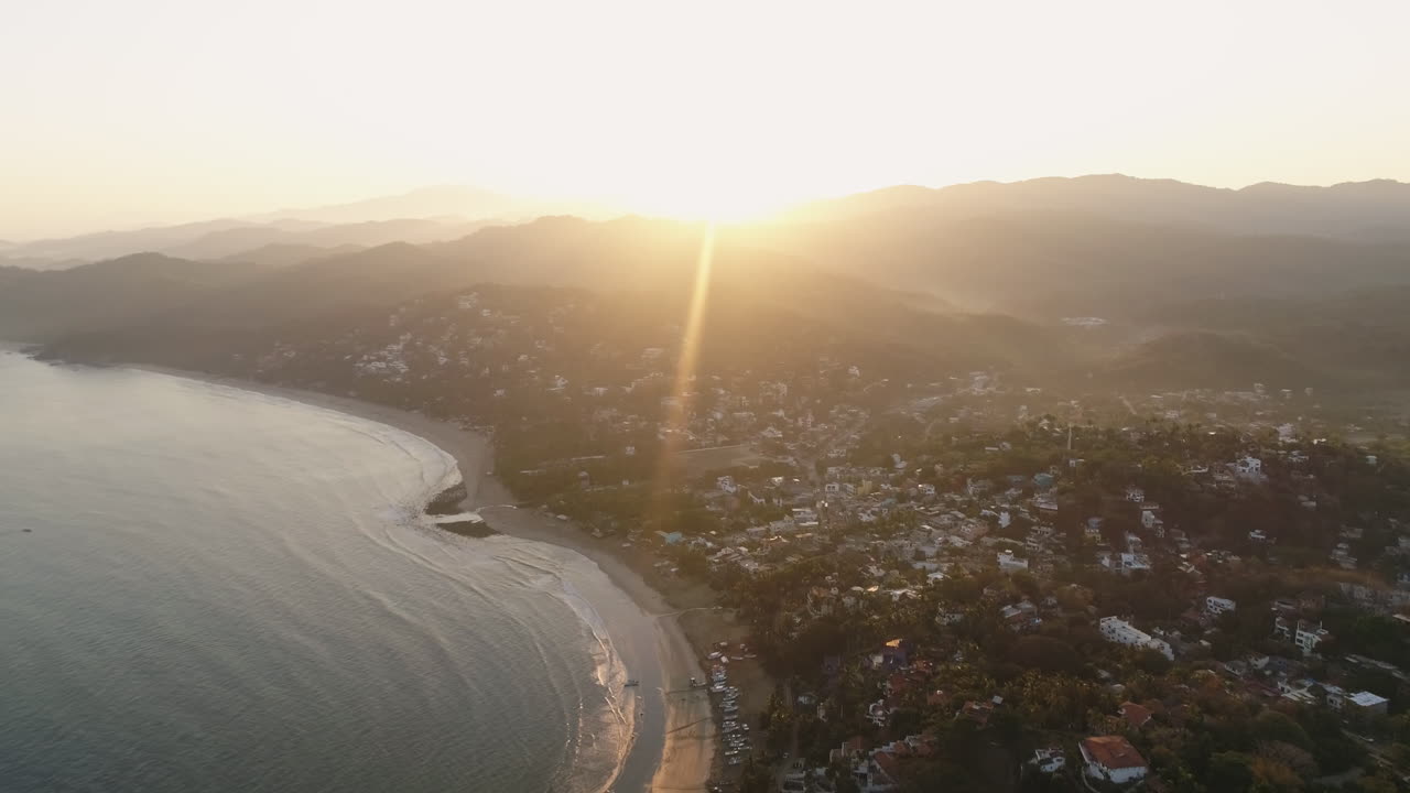 amplia antena de amanecer con destellos de sol sobre una pequeña ciudad de surf costera mexicana, 4k