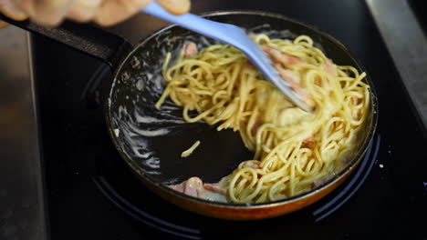 frying pasta with bacon in tasty sauce. cooking tasty dish in a frying pan. chef cooks spaghetti pasta in a restaurant kitchen. food ingredient. cooking on cuisine. cooked for gourmet.