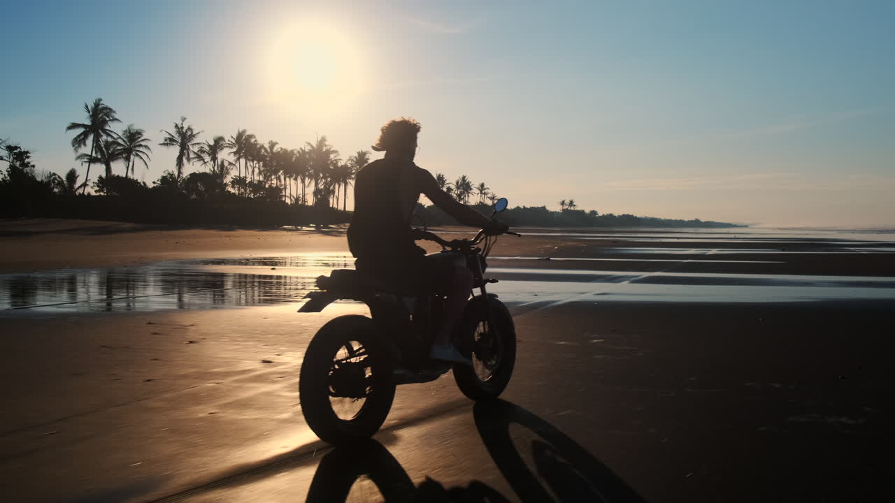Man riding motorcycle on a beach at sunrise/sunset