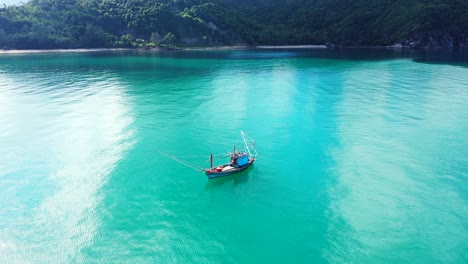 fishing boat floating on calm turquoise lagoon near coastline of tropical island with rocks and beaches of green hills