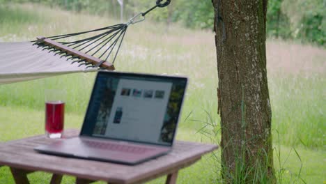 homeoffice setting with laptop on table in garden next to hammock, pan