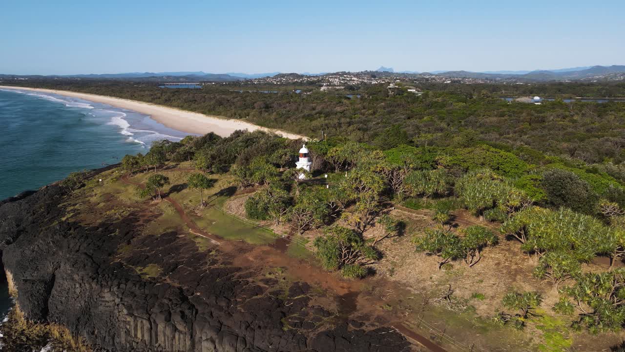 토착 식물과 산을 배경으로 둘러싸인 험준한 해안 곶에 자리 잡은 유서 깊은 등대의 모습을 드러냅니다.