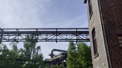 old-brick-building-newly-renovated-on-the-grounds-of-the-landscape-park-duisburg-in-germany-with-old-historical-industrial-plants-with-rusty-pipes-behind-nature-on-the-horizon