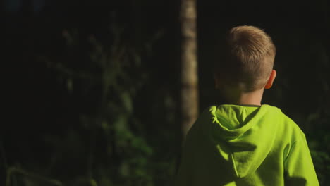 un niño alegre camina con su familia por el bosque disfrutando del fin de semana en la naturaleza. niño en ropa deportiva cómoda juega y se divierte en la noche en los arbustos iluminados