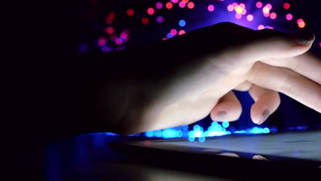 woman hand touching and browsing on tablet device in dark room with colorful blurry fiber optic lights closeup panning motion