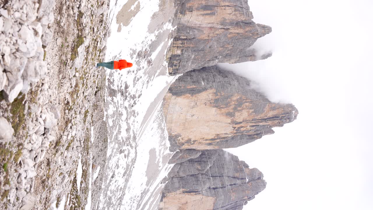 mujer con capucha naranja en medio de árboles nevados cime di lavaredo, la niebla oculta los picos