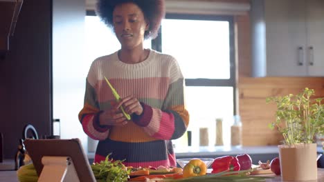 african american woman preparing meal using tablet in sunny kitchen