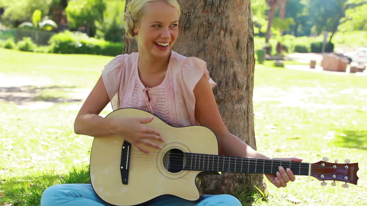 En kvinna sitter vid ett träd och spelar gitarr