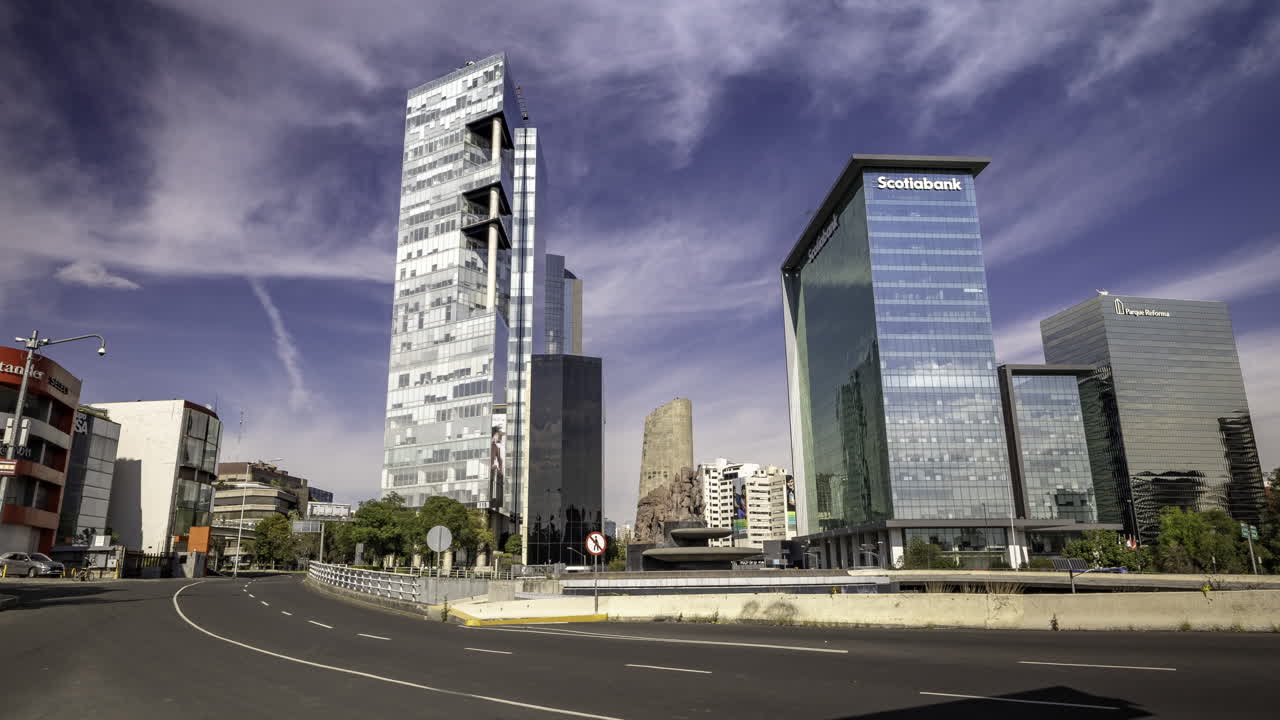 tomada panorámica de la fuente de petroleos en la avenida paseo de la reforma con varios edificios de oficinas en el fondo en un día soleado en la ciudad de méxico, varios vehículos pasan delante de ella en la calle