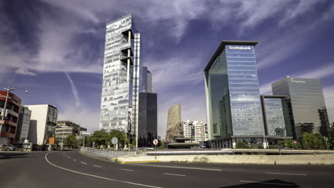 panoramic shot of the petroleos fountain on paseo de la reforma avenue with several office buildings in the background on a sunny day in mexico city, several vehicles pass in front of it on the avenue