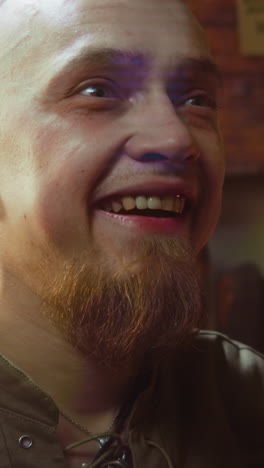 hombre barbudo con una amplia sonrisa en la taberna de primer plano. tipo emocionado ver el artículo buscado en la tienda medieval. invitado del pub tonto mira hacia adelante después de varios disparos