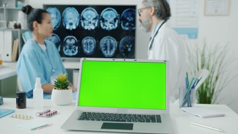 el médico hablando con la enfermera discutiendo las exploraciones de resonancia magnética mientras la pantalla verde de la llave de croma de la computadora portátil visible en primer plano