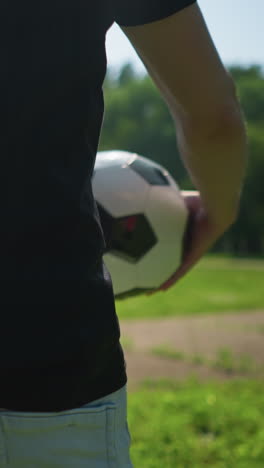 una vista en primer plano de un hombre girando una pelota de fútbol a su alrededor, con un fondo borroso que muestra a otras personas y un niño caminando