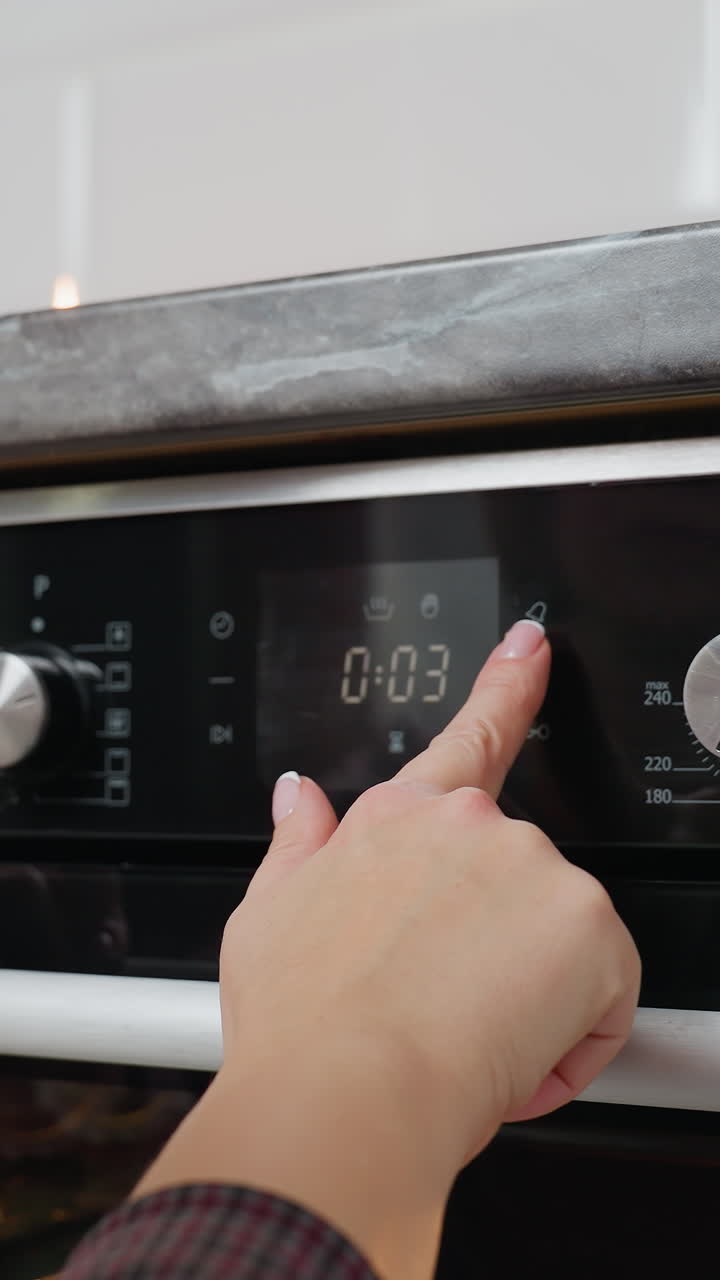 Primo piano di una donna che utilizza i comandi digitali di un forno, regolando la temperatura o il timer in una cucina moderna con tecnologia avanzata per cuocere biscotti o preparare cibo