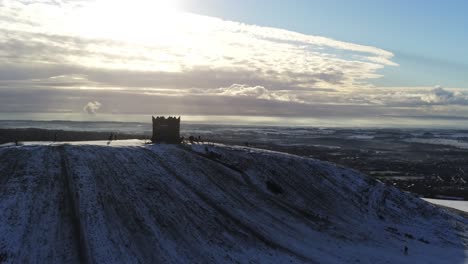 snowy rivington pike tower winter hill vista aérea gente en trineo cuesta abajo al amanecer empujón lento sobre la torre