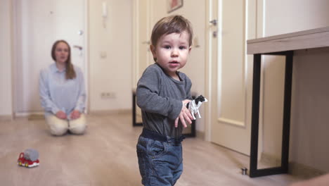 baby looking at camera while holding a toy standing in the corridor at home