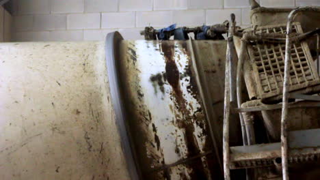 close-up of a dirty industrial cement mixer and wheelbarrow at a construction site, showing texture, rust, and signs of heavy use inside a workshop or warehouse