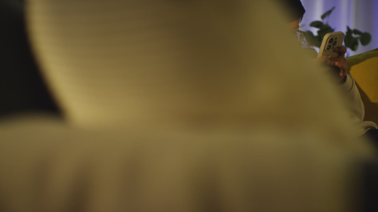 Young Boy Sitting On Sofa In Lounge At Home Playing Game On Mobile Phone At Night 3