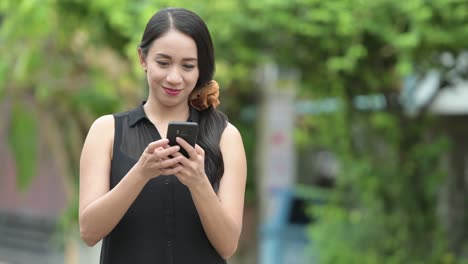 young beautiful asian businesswoman using phone in the streets outdoors