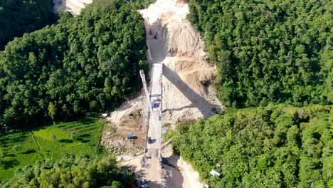 heavy equipment building bridge over valley in indonesia forest area, aerial view