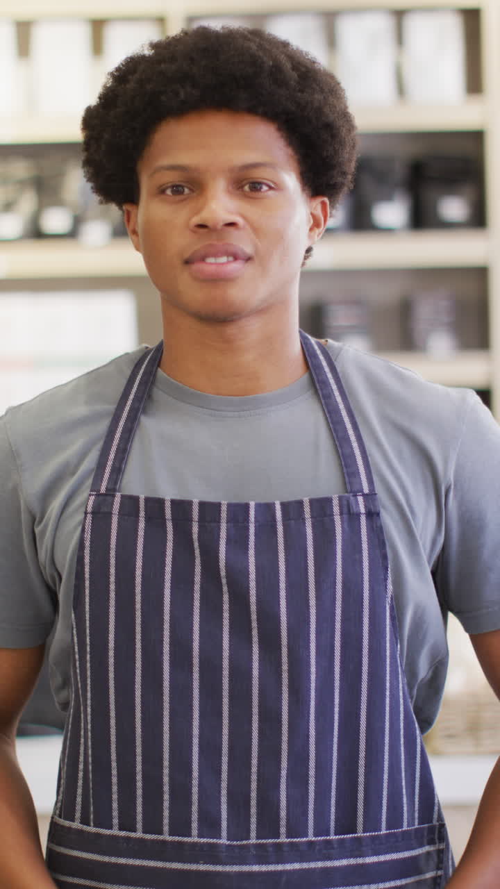 vídeo vertical de um barista afro-americano sorridente usando avental em um café