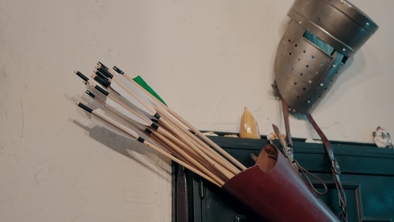 Medieval style arrows in a leather quiver with a helmet hanging on the wall