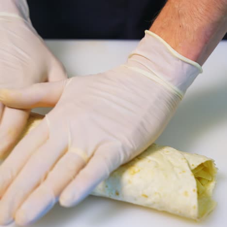 cooking meat and cheese shawarma. hands in latex gloves roll up a pita roll. close-up