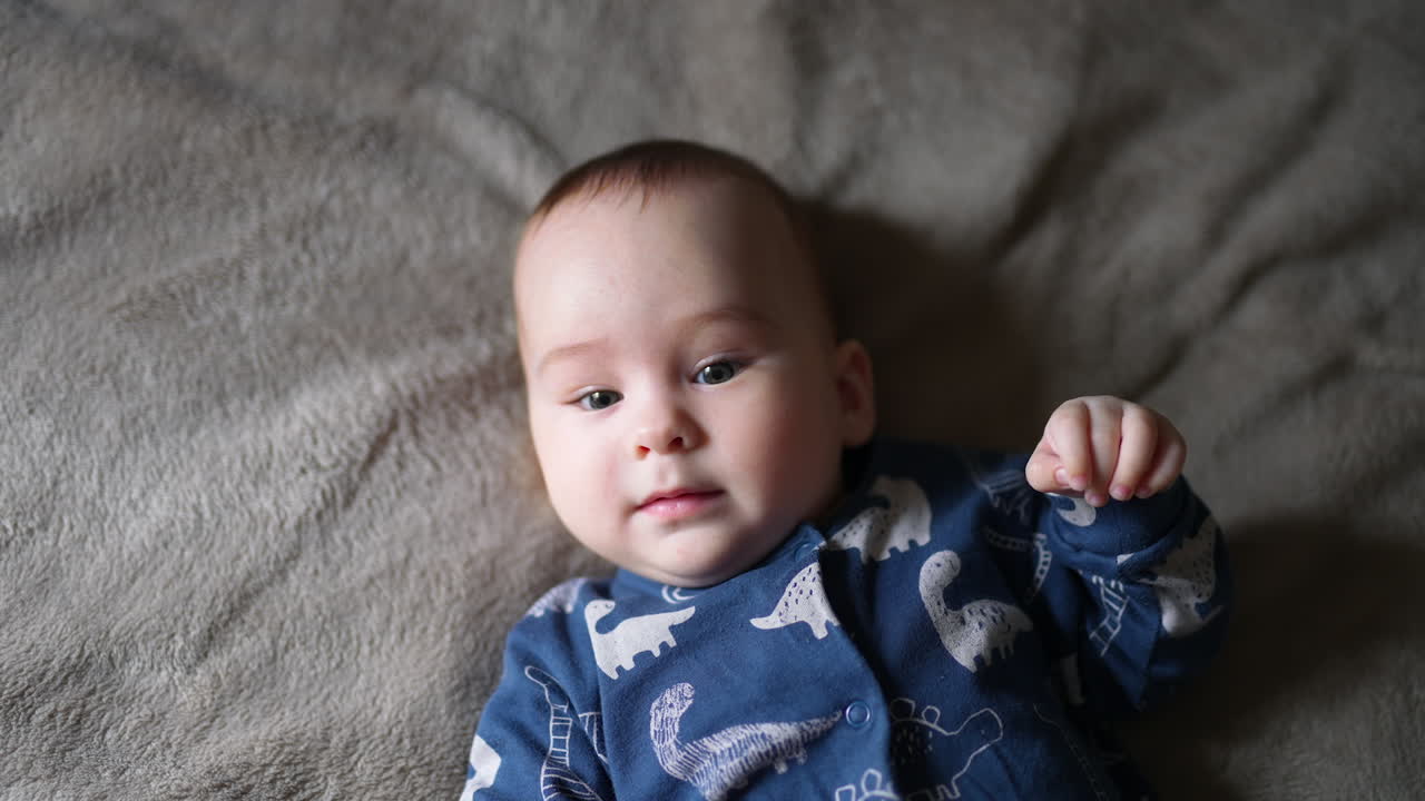 Beautiful toddler boy lies on bed looking into camera with interest. Sweet child upper body part close up.