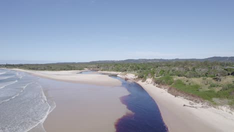 tea-tree stained fresh water of belongil creek flowing into the sea at the belongil beach in new south wales, australia