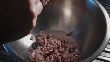 chef adding canned tuna into an empty metal bowl to begin preparing a tuna salad