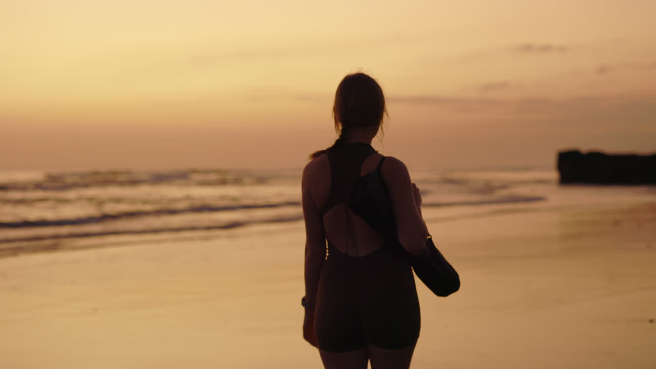 Woman with yoga mat on beach at sunset