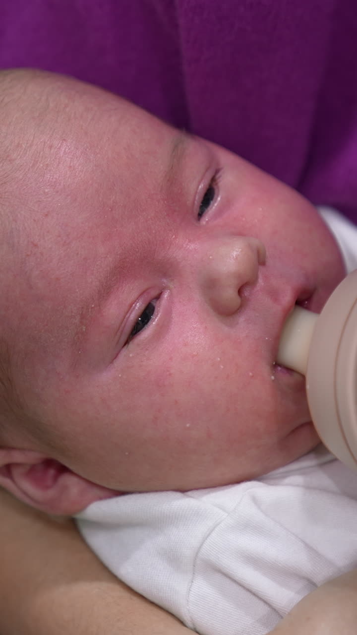 Adorable child in mother's hands ready to have meal. Little kid refuses to take the bottle first but then takes it and starts to eat. Close up. Vertical video