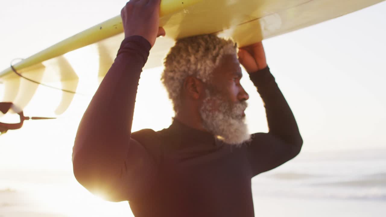 Älterer afroamerikanischer Mann geht mit Surfbrett am sonnigen Strand