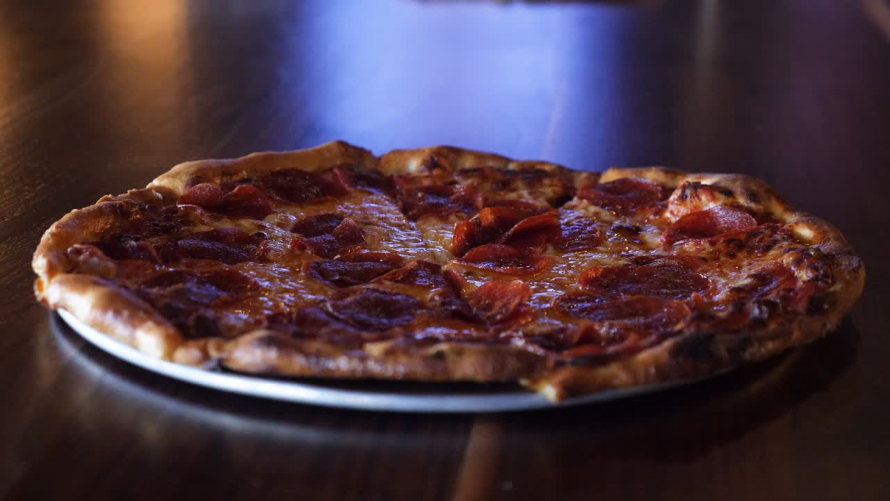 Primo piano di una deliziosa pizza su un tavolo di legno al rallentatore