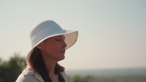 close up of adventurous woman adjusting camera lens while gazing at hazy countryside from sunlit hilltop, soft breeze moving hair, serene exploration mood in warm light over rolling meadow