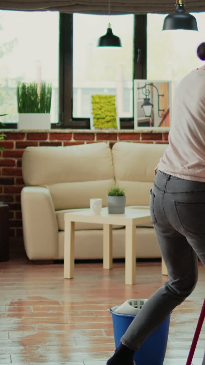 Vertical video: Happy funny person mopping floors with all purpose cleaner and dancing