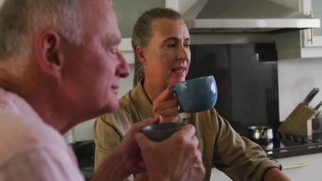 Caucasian-senior-couple-holding-coffee-cup-talking-to-each-other-in-the-kitchen-at-home