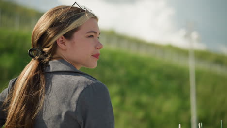 close-up of a thoughtful lady in a grey top with sunglasses resting on her head, looking away into the distance, seated outdoors