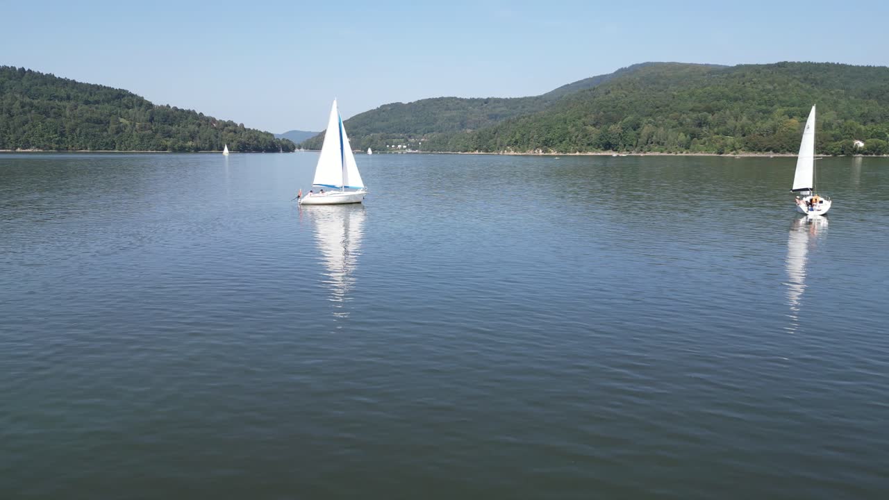 barcos de vela en el lago tranquilo en las montañas beskid, rodeados de vegetación durante un día de verano perezoso - vista aérea de avión no tripulado 4k
