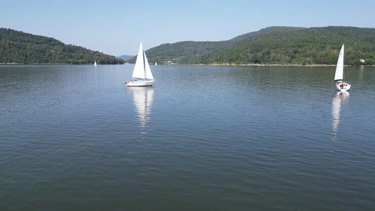 Sailing boats at calm lake in Beskid mountains, surrounded by greenery during a summer lazy day - drone aerial view 4K