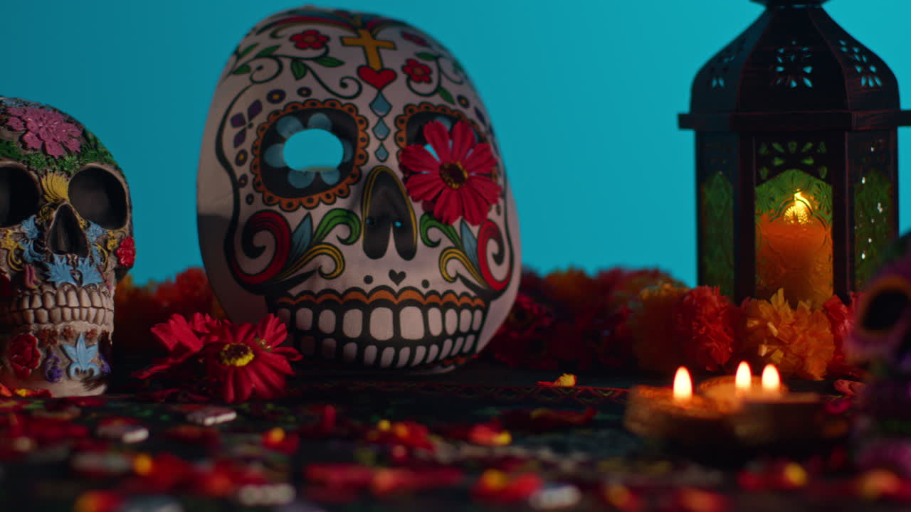 close up de cráneos y máscaras decoradas rodeadas de velas y pétalos de flores celebrando la fiesta mexicana de dia de muertos o día de los muertos contra fondo azul 2